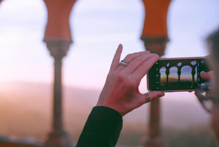 An illustrative photo of an anonymous lady photographing an arched palace at sundown