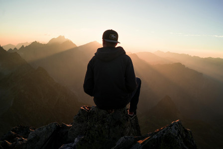An illustrative photo of a man sitting on the mountain edge.