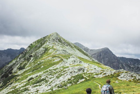 An illustrative photo of two people walking on a hill under white clouds
