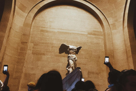 An illustrative photo of tourists taking a photo of an ancient sculpture in a museum