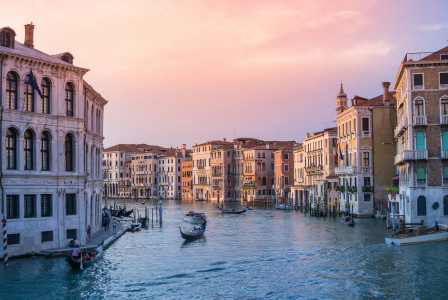 An illustrative photo of gondolas on body of water between buildings during sunset