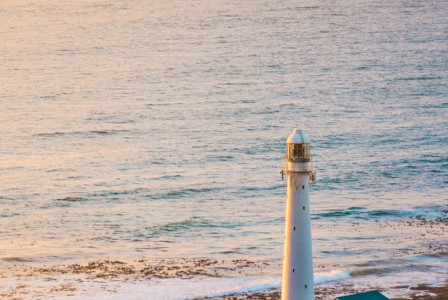 An illustrative photo of a tall white lighthouse, standing near the edge of a coastline