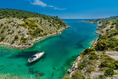 An illustrative photo of white boat near body of water between green mountains