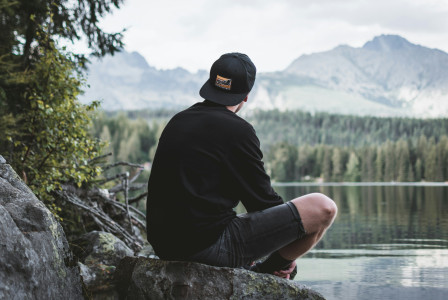 An illustrative photo of man sitting on rock while looking at mountains.