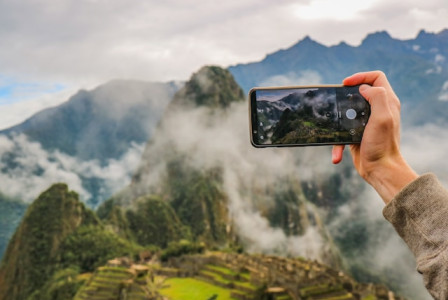 An illustrative photo of a person holding smartphone taking picture of green mountain.