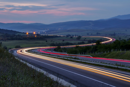 An illustrative photo of a highway at dusk or early evening, capturing the light trails of vehicles