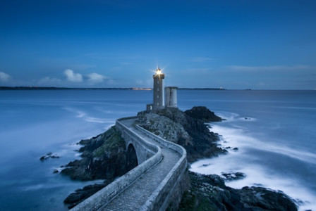 An illustrative photo of a gray lighthouse standing resolutely on a small islet, connected to the mainland by a concrete pathway