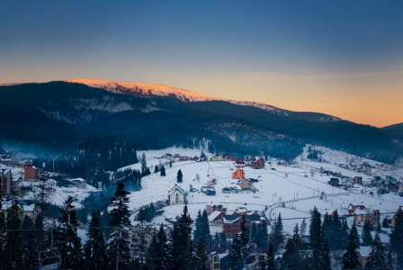 An illustrative photo of snowy mountain surrounded of larch trees.