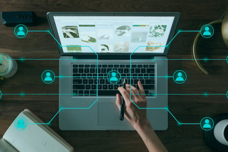 Photo by Pixabay An illustrative photo of a person using a laptop on a wooden desk, surrounded by various objects and digital graphics