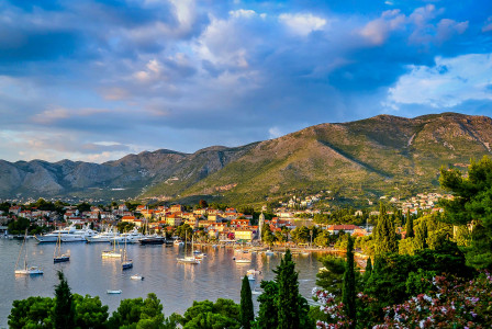 An illustrative photo of boats on body of water surrounded by trees and houses near mountain