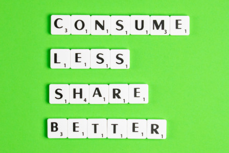 An illustrative photo of white tiles with black letters spelling out the phrases “CONSUME LESS,” “SHARE MORE,” and “LIVE BETTER” against a bright green background