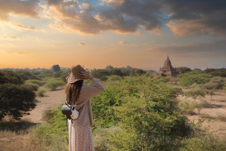 An illustrative photo of a woman wearing a straw hat and a dress, taking a photograph of a landscape