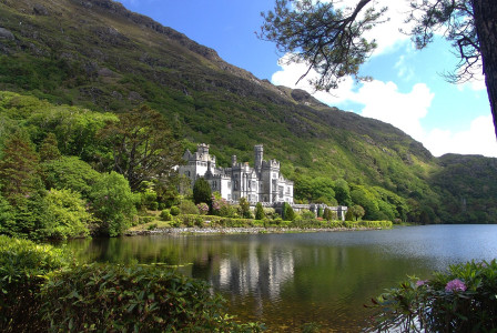 An illustrative photo of a grand white castle with multiple towers and windows, nestled among green hills and reflected in the calm waters of a lake