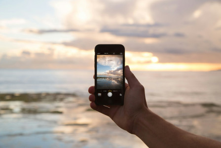 An illustrative photo of a person holding smartphone showing ocean.