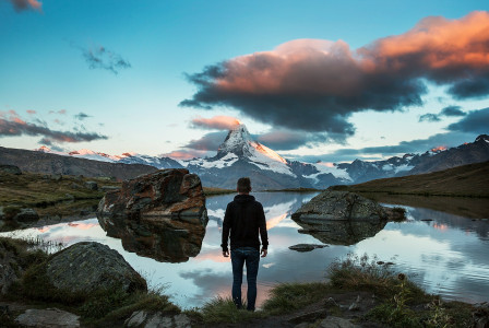 An illustrative photo of man standing on rocky cliff facing body of water.