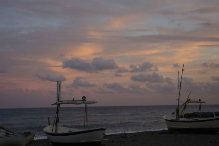 An illustrative photo of a couple of boats sitting on top of a beach during sunset