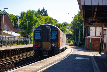 An illustrative photo of a train at a station platform during daylight, surrounded by infrastructure and greenery