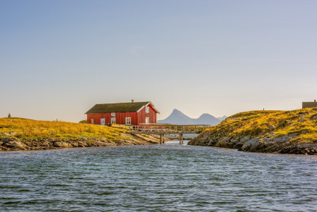 An illustrative photo of a red house on a grassy coastline with a bridge in the background
