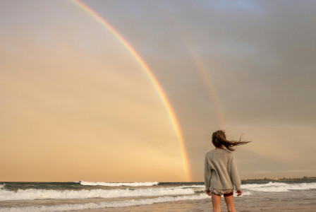 An illustrative photo of a woman standing on shore with rainbow