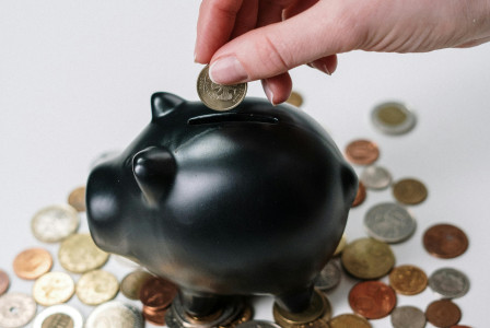 An illustrative photo of a person putting coin in a piggy bank