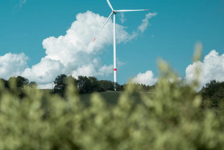 An illustrative photo of a single wind turbine stands tall on a field against a clear blue sky