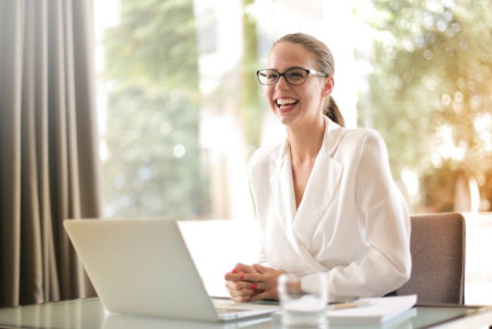An illustrative photo of a businesswoman laughing while working on her laptop in an office