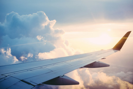 An illustrative photo of an airplane wing in the sky with clouds