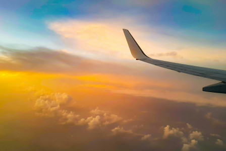 An illustrative photo of a white airplane wing above white clouds with sunset or sunrise
