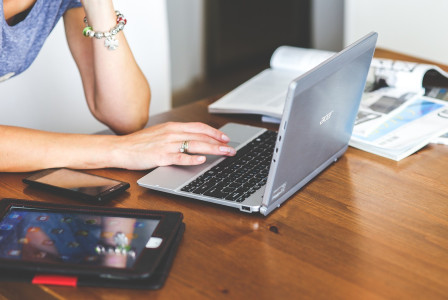 An illustrative photo of a person working on the laptop with a phone and a tablet on the table