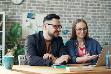 An illustrative photo of a man and a woman sitting at a table looking at a laptop