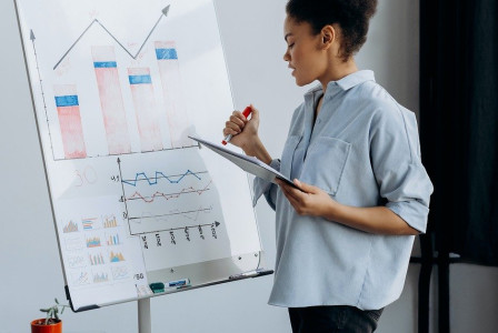 An illustrative photo of a woman standing next to a whiteboard with various charts and graphs
