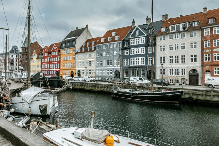An illustrative photo of a river with boats under cloudy sky near colorful buildings