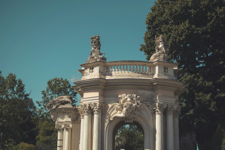 An illustrative photo of  a white arch with statues on top of it near green trees