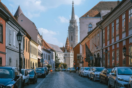 An illustrative photo of cars parked on the narrow street between brown concrete buildings.