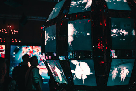 An illustrative photo of a group of people standing around a display of video screens