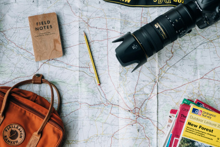An illustrative photo of a camera, a book, and a bag on a map