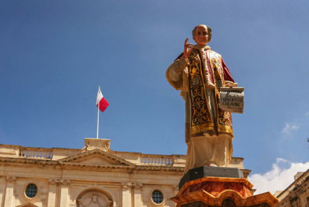 An illustrative photo of a statue of a priest in front of a building in Malta