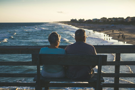 An illustrative photo of old man and woman sitting on bench in front of beach