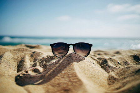 An illustrative photo of a black Ray-Ban Wayfarer sunglasses on beach sand
