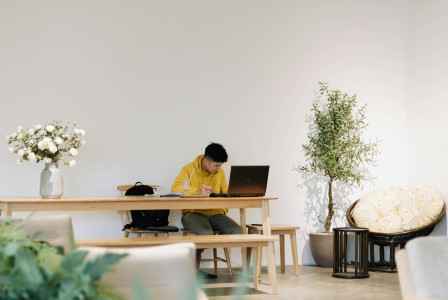 An illustrative photo of a man in yellow shirt sitting on chair in front of laptop computer
