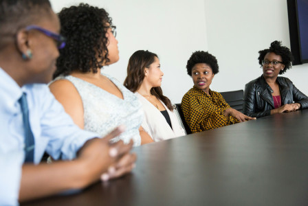 An illustrative photo of five people sitting at table and talking