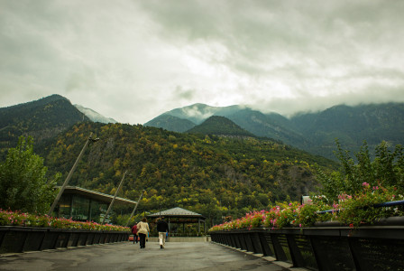 An illustrative photo of people walking on wooden bridge near green mountains