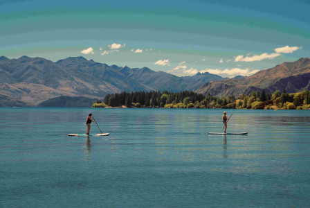 An illustrative photo of two people riding on paddle boards in a lake near mountains.