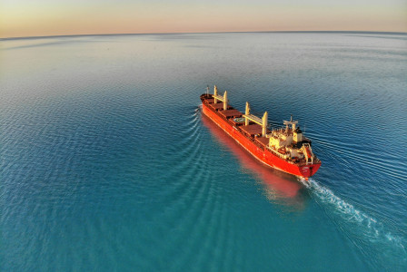 An illustrative photo of a red and white cargo ship at middle of ocean