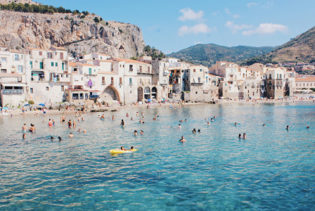 An illustrative photo of people swimming in a sea near a beach with buildings