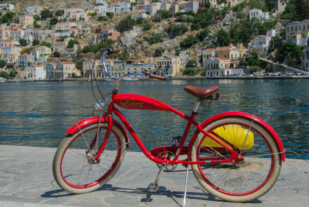 An illustrative photo of a red bicycle near a body of water with a city in the background