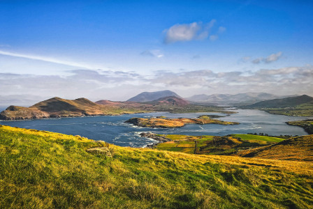 An illustrative photo of a green grass field near body of water under blue sky.