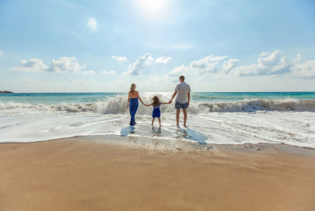 An illustrative photo of a man, a woman and a child holding hands on a seashore.