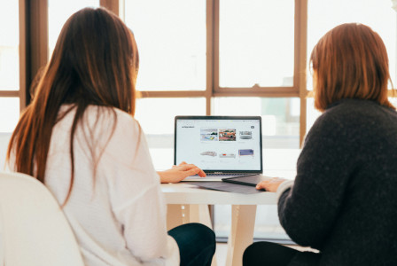 An illustrative photo of two women talking while looking at laptop computer.
