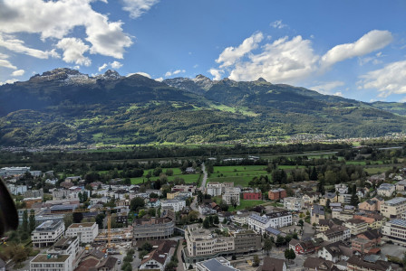An illustrative photo of city buildings and green mountains.